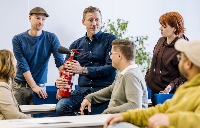 Praxisnahe Schulung zum Brandschutzbeauftragten: Dozent demonstriert Einsatz eines Feuerlöschers im Seminarraum - fundierte Ausbildung mit direktem Anwendungsbezug.