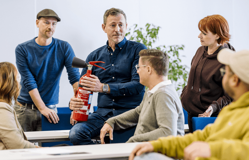 Praxisnahe Schulung zum Brandschutzbeauftragten: Dozent demonstriert Einsatz eines Feuerlöschers im Seminarraum - fundierte Ausbildung mit direktem Anwendungsbezug.