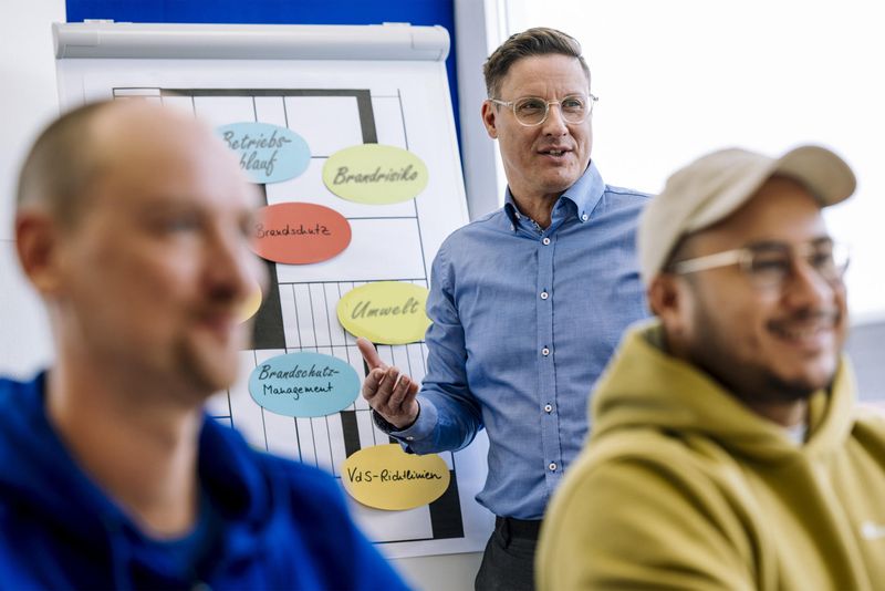 Trainer erläutert zentrale Aspekte des Brandschutzmanagements vor Flipchart mit Schlagworten wie Betriebsablauf, Brandrisiko-Management und Brandschutzprozesse – praxisnahe Fortbildung zur Optimierung innerbetrieblicher Sicherheitsprozesse.